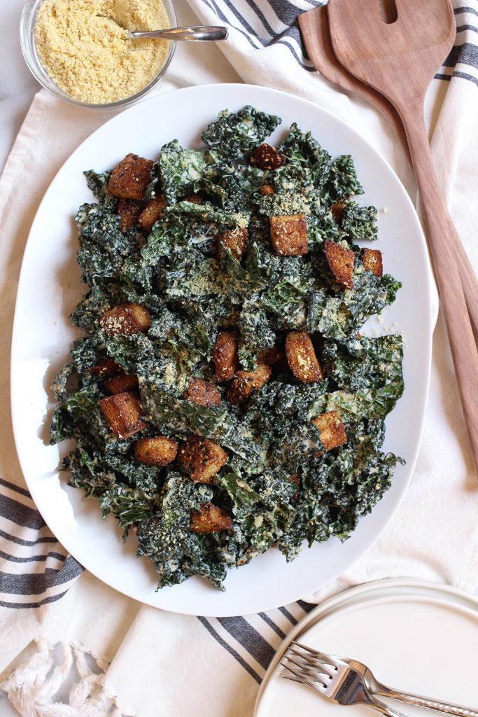 Vegan Kale Caesar Salad with tangy garlic tahini dressing, cashew parmesan, and whole grain croutons.