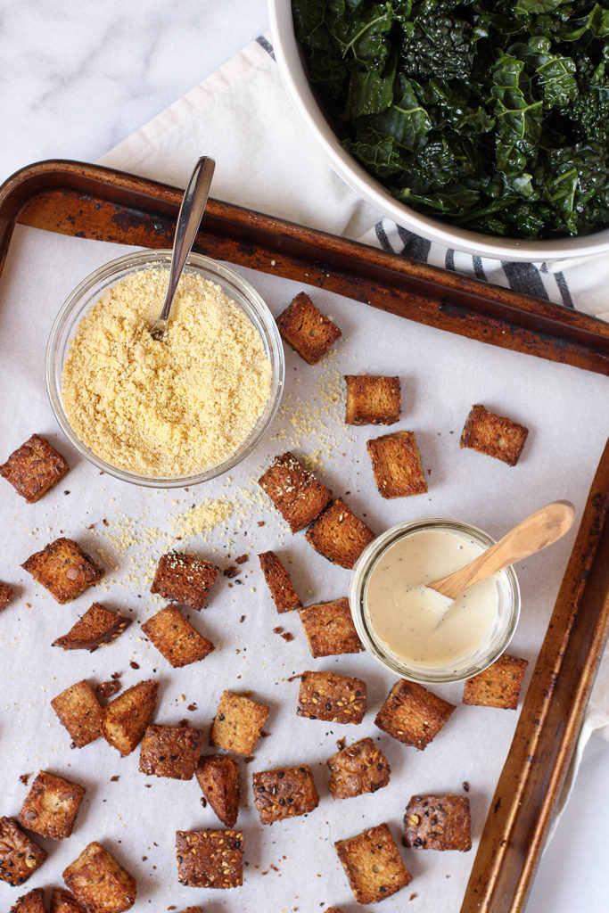 Vegan Kale Caesar Salad with tangy garlic tahini dressing, cashew parmesan, and whole grain croutons.