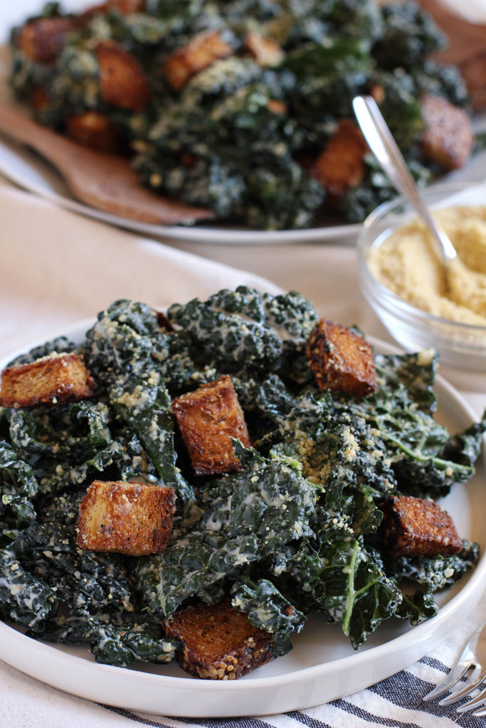 Vegan Kale Caesar Salad with tangy garlic tahini dressing, cashew parmesan, and whole grain croutons.